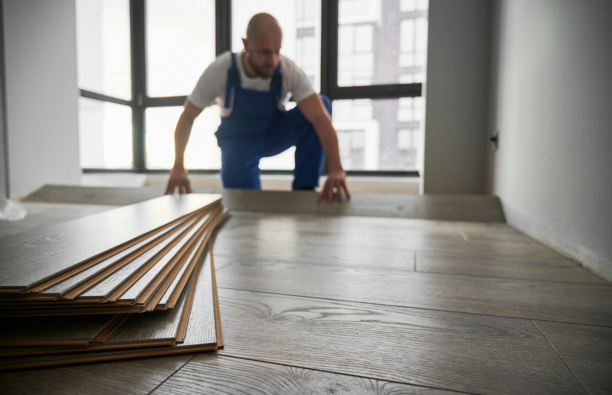Laminate planks and male flooring installer on background.